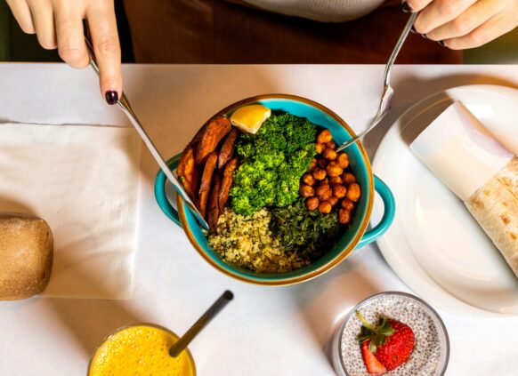 Colorful vegetarian meal bowl with chickpeas, broccoli, quinoa, sweet potato, greens, wrap, and chia pudding on a table.