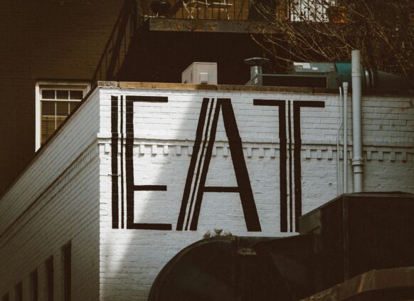 Wall mural with bold black letters spelling "EAT" on a white brick building.
