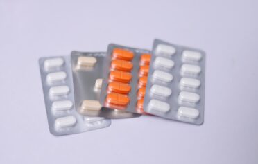 Various blister packs containing white, beige, and orange tablets on a light background