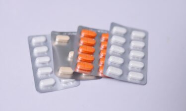 Various blister packs containing white, beige, and orange tablets on a light background