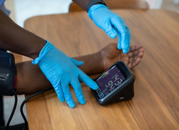 Healthcare worker in blue gloves checking a patient's blood pressure with a digital monitor on a wooden table