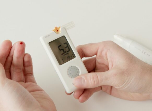 Person checking blood sugar levels with a glucometer showing 5.3 mmol/L and a drop of blood on fingertip