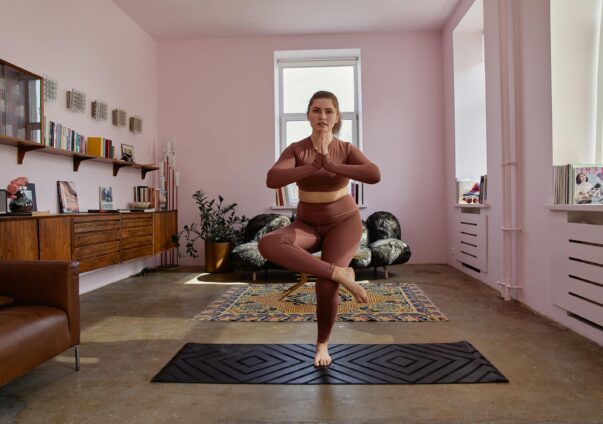 Woman in activewear practicing yoga in tree pose on a mat in a stylish living room