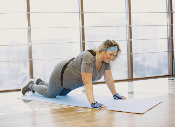 Smiling woman in activewear doing modified push-ups on a yoga mat in a bright gym
