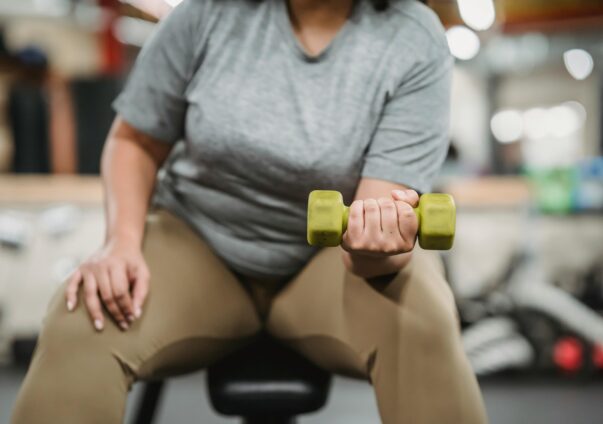 Person in gym clothes lifting a green dumbbell while seated on a bench