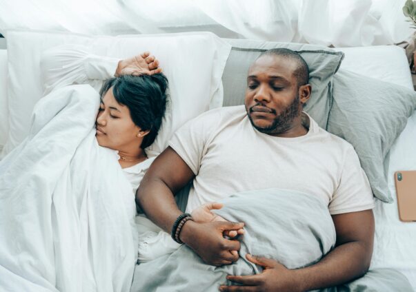 Couple peacefully sleeping in bed while holding hands, covered in white and grey bedding
