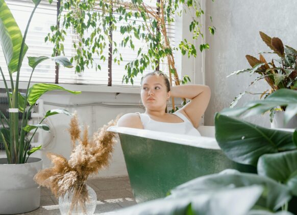 Woman in a green bathtub surrounded by indoor plants in a sunlit room
