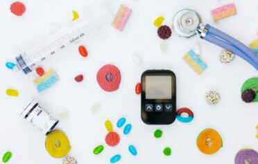 Medical devices including glucose meter, syringe, and candies on white background.