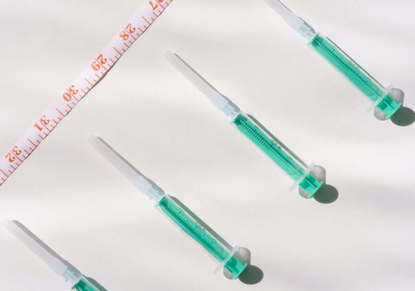 Flat lay of green syringes and a measuring tape on a white background, symbolizing weight loss or medical treatment