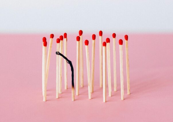 Group of unlit red-tipped matches surrounding one burned-out matchstick on a pink background.