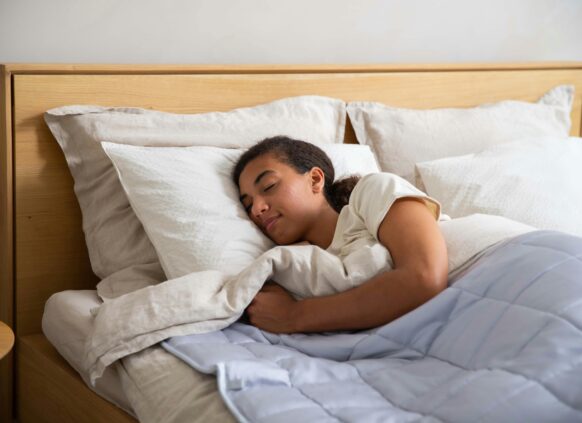 Young woman sleeping peacefully in bed with white pillows and a soft comforter.