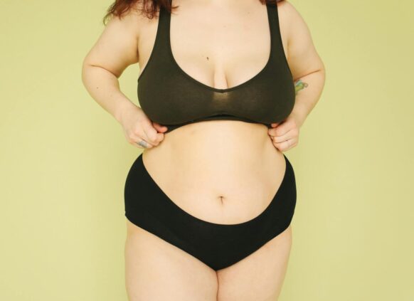 Plus-size woman in underwear adjusting her sports bra against a light green background