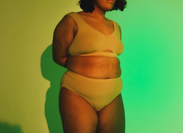 Plus-size woman standing confidently in underwear, showing natural skin texture and stretch marks under soft lighting.