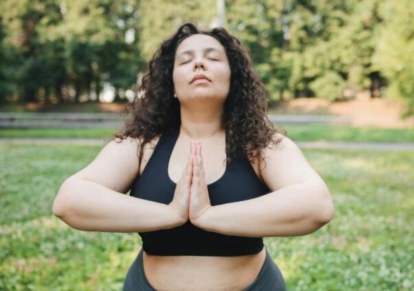Curly-haired woman practicing yoga outdoors with eyes closed and hands in prayer position