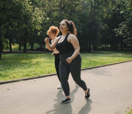 Two women in activewear jogging on a park path surrounded by greenery