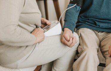 Elderly woman measuring a man's blood pressure at home using a digital monitor