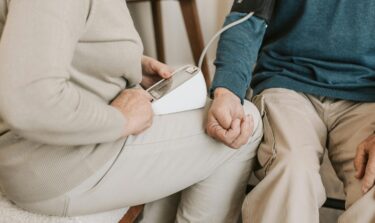 Elderly woman measuring a man's blood pressure at home using a digital monitor
