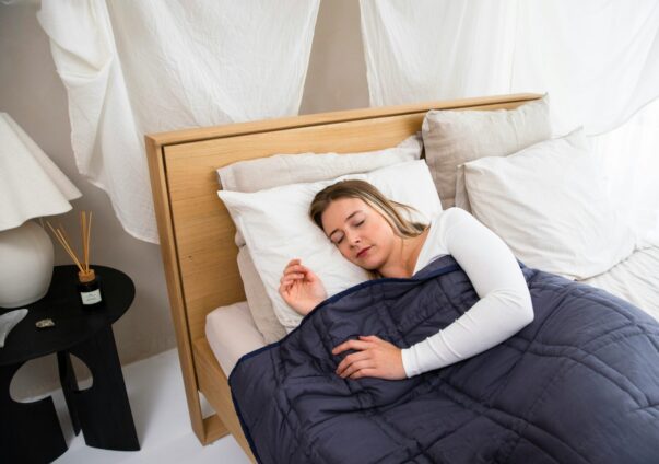 Woman peacefully sleeping in a cozy bed with a dark blue blanket and white pillows in a softly lit room