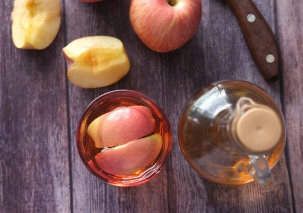 Fresh apples with apple cider vinegar in a glass and jug on a rustic wooden table.