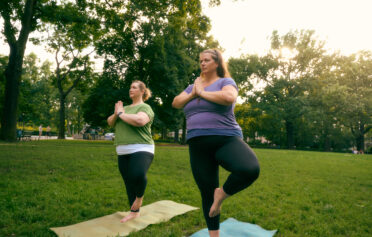 Two women doing yoga on the grass in a park