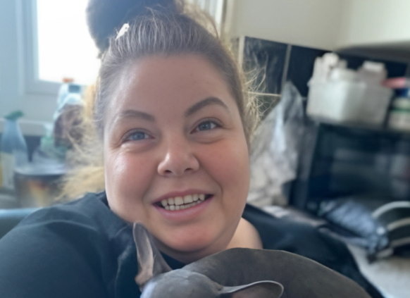 Smiling woman at home holding a small dog in her arms.