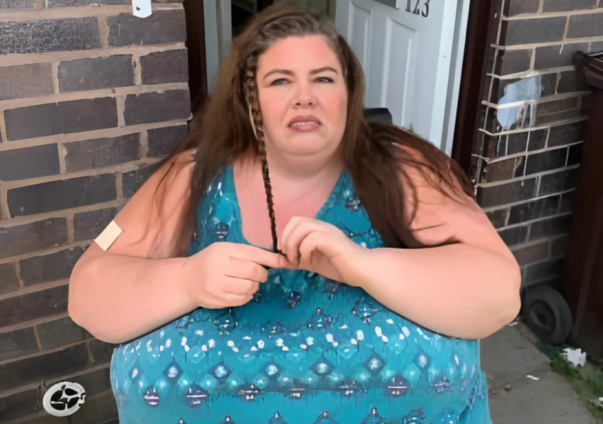Woman sitting outside on a doorstep, braiding her hair in a blue patterned dress.