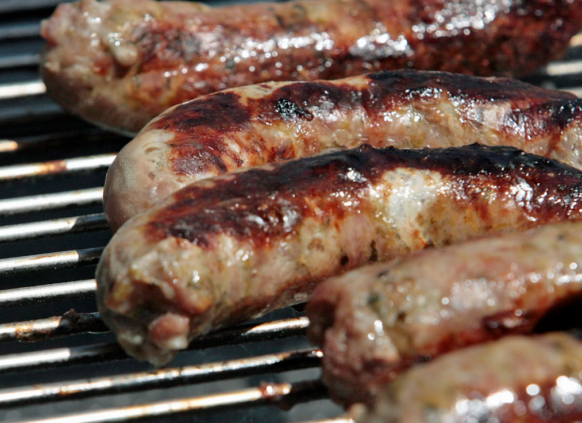 Grilled sausages sizzling on a barbecue with visible fat and char marks