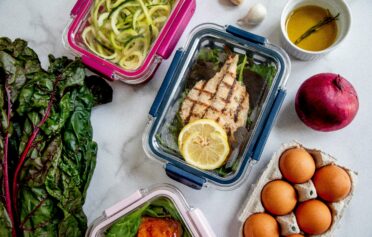 Meal prep containers with grilled chicken, vegetables, eggs, and healthy ingredients on a white surface
