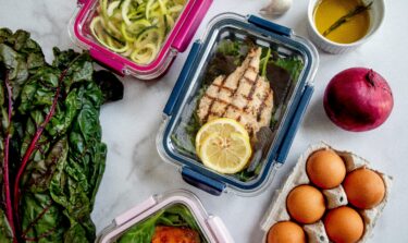 Meal prep containers with grilled chicken, vegetables, eggs, and healthy ingredients on a white surface