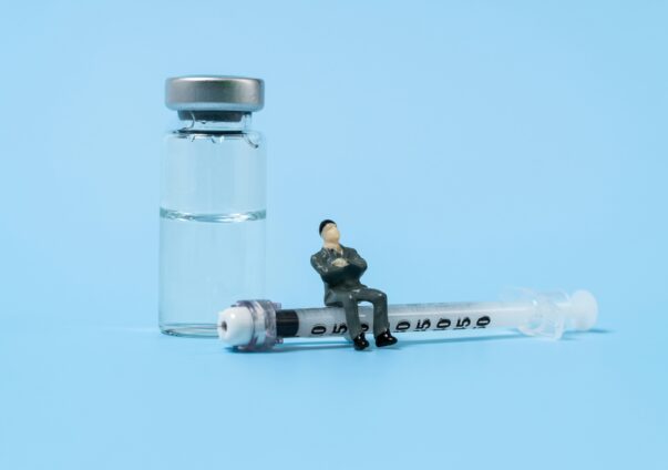 Miniature figure sitting on a syringe next to a vial, symbolizing retatrutide injection
