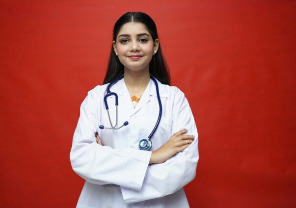 Confident female doctor in a white coat with stethoscope standing against red background