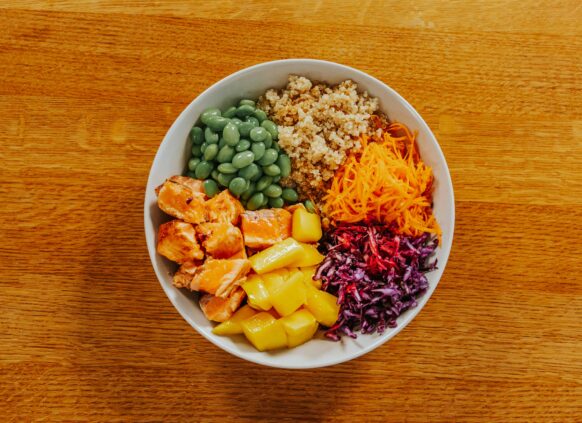 Colorful healthy bowl with salmon, quinoa, edamame, mango, shredded carrots, red cabbage, and beets