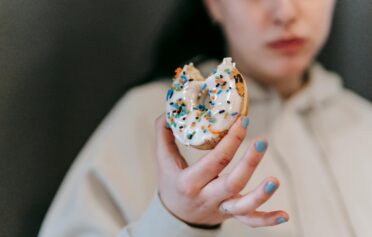 Person holding a bitten donut with white icing and colorful sprinkles