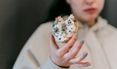 Person holding a bitten donut with white icing and colorful sprinkles