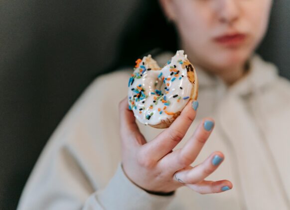 Person holding a bitten donut with white icing and colorful sprinkles