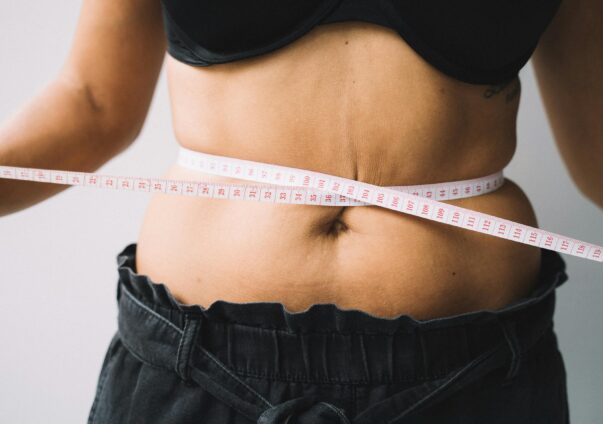 Woman measuring waist with tape measure as part of weight loss progress.