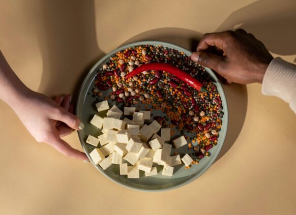 Mixed legumes, tofu cubes, and red chili pepper on a plate held by two hands