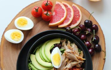 Healthy lunch bowl with avocado, egg, chicken, tomatoes, cherries, and grapefruit slices on a wooden plate