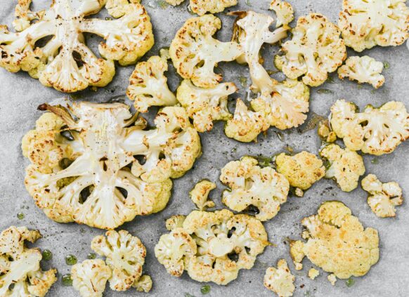 Roasted cauliflower slices on a baking tray with olive oil and seasoning.