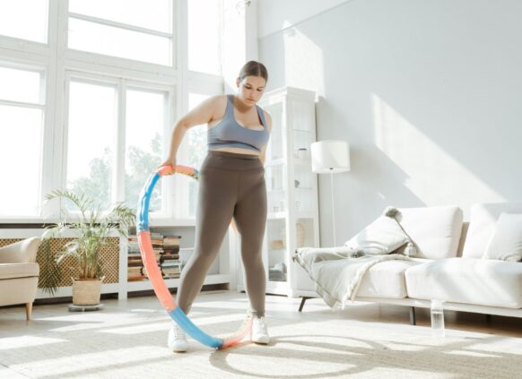 Young woman using a weighted hula hoop for fitness exercise at home.