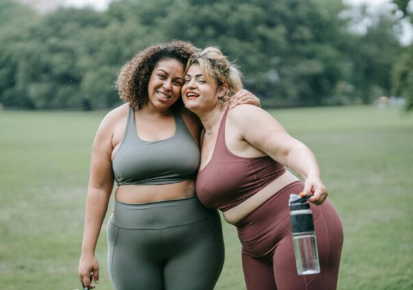 Two plus-size women in activewear smiling together outdoors after exercise.