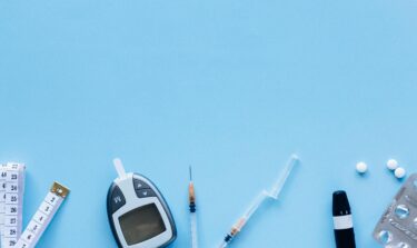 Medical tools for diabetes management including glucometer, syringe, pills, and measuring tape on blue background.