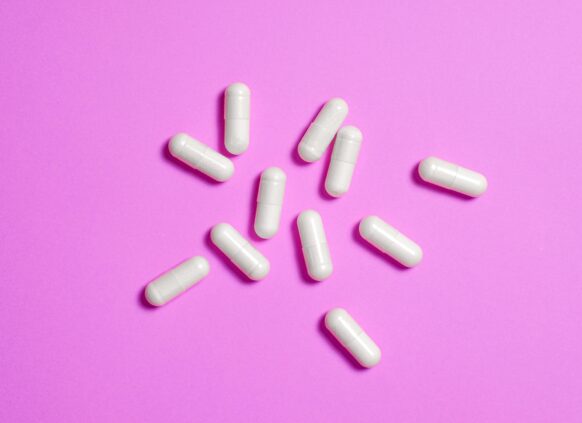 White weight loss capsules arranged in a circular pattern on a pink background.