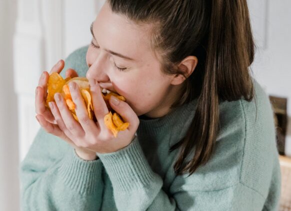 Woman in sweater emotionally eating chips in large handfuls