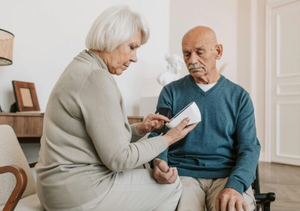 Elderly woman checking elderly man’s blood pressure with digital monitor at home.
