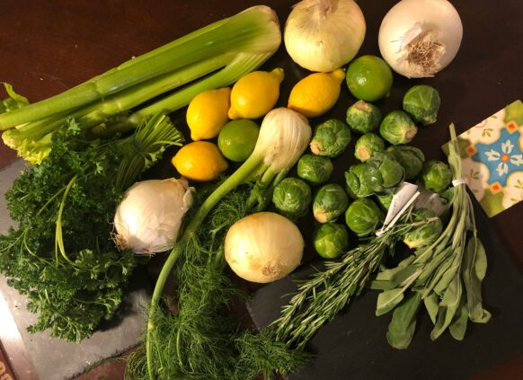 Assorted fresh vegetables and herbs including celery, lemons, onions, Brussels sprouts, and parsley on a kitchen counter