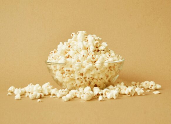 Glass bowl of popcorn with scattered kernels on beige background