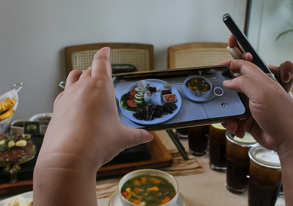 Hands taking a smartphone photo of a plated meal at a restaurant table.
