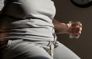 Overweight person in grey loungewear holding a glass of water