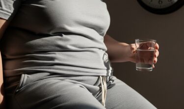 Overweight person in grey loungewear holding a glass of water